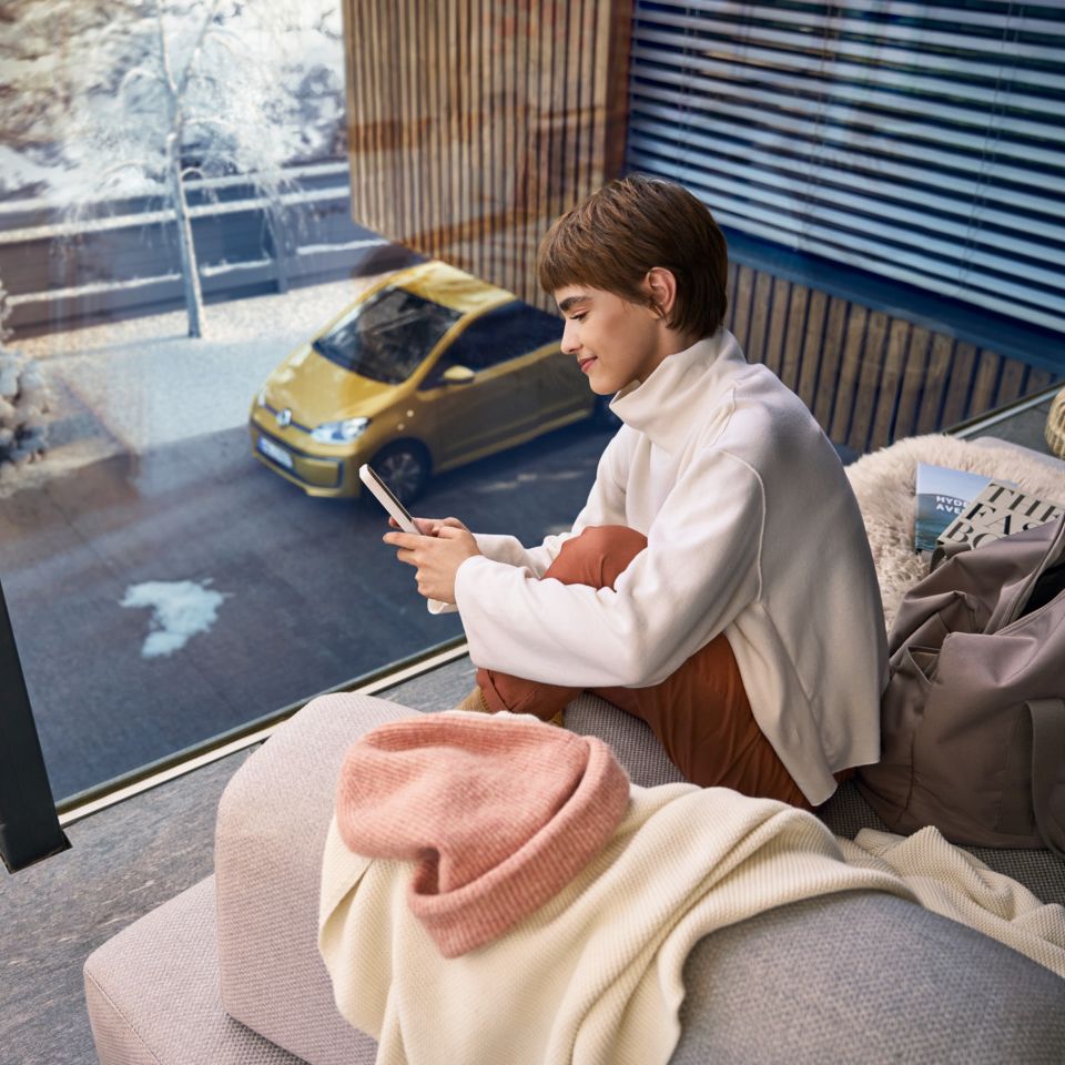 Frau sitzt auf dem Balkon und verbindet sich über das Handy mit ihrem e-up! 