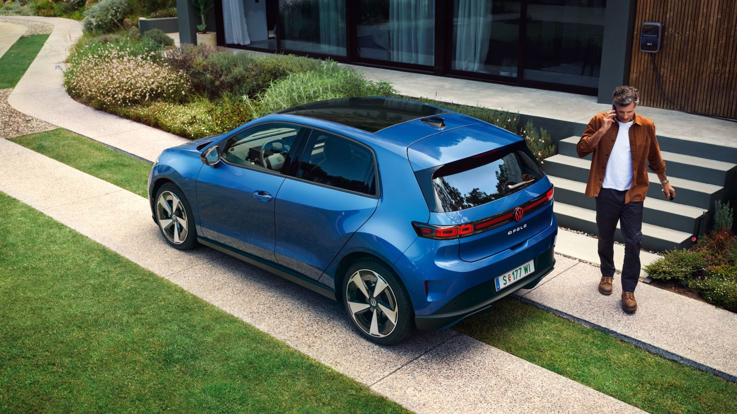 Modri VW ID. Polo Style je parkiran pred zeleno stanovanjsko stavbo, za vozilom hodi moški.