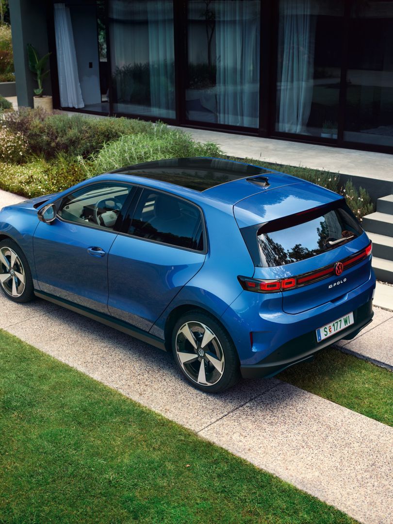 Modri VW ID. Polo Style je parkiran pred zeleno stanovanjsko stavbo, za vozilom hodi moški.