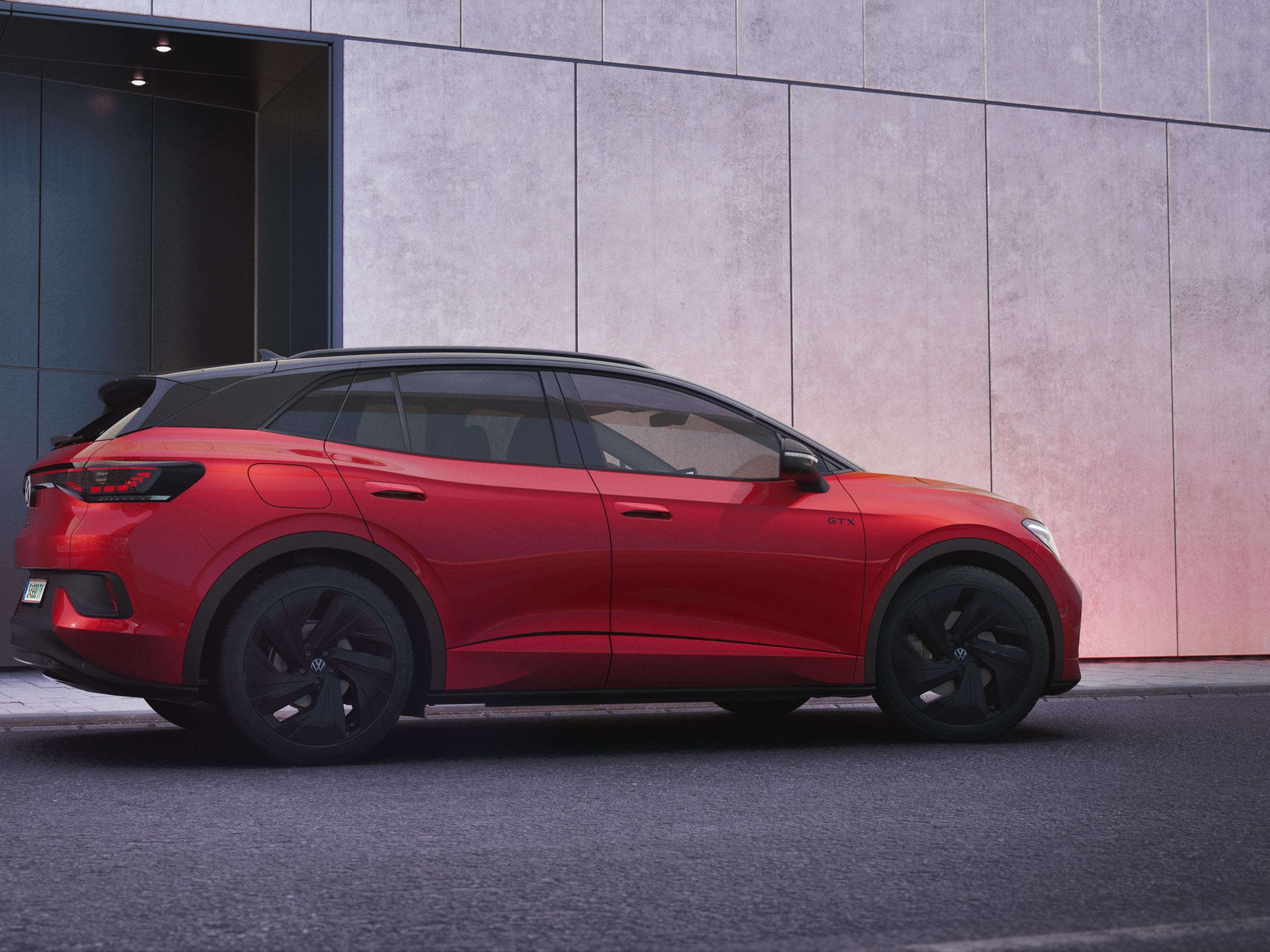 Ein roter VW ID.4 GTX in der schräg seitlichen Heckansicht vor einer schwarz-grauen Hauswand.