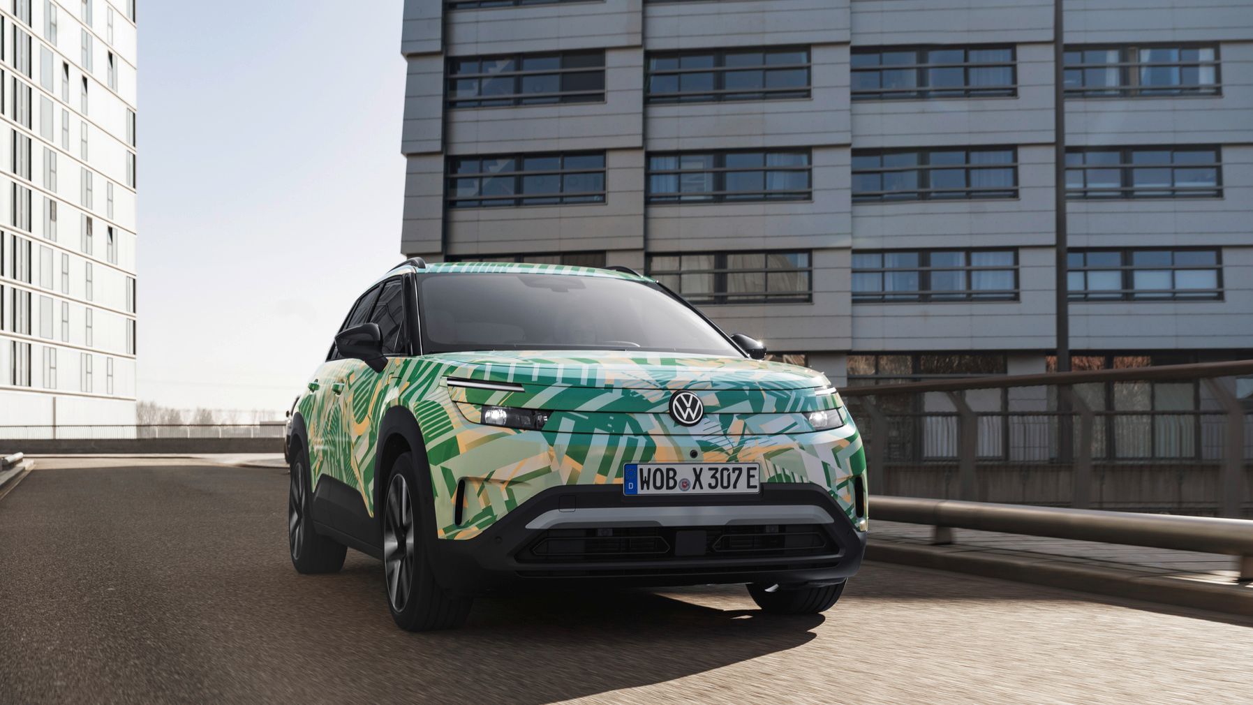 VW ID. Cross z maskirno folijo na mestni parkirni ploščadi pred sodobno stolpnico.