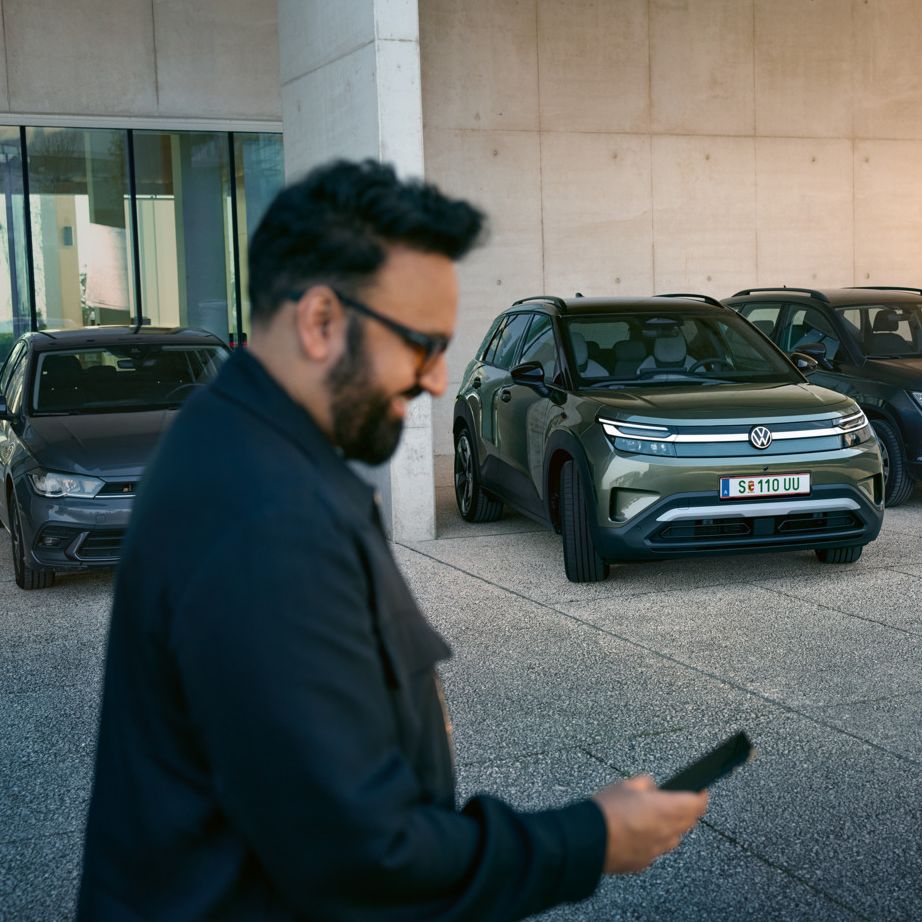 Moški gleda na svoj pametni telefon, v ozadju VW ID. Cross samodejno zapelje na parkirno mesto.
