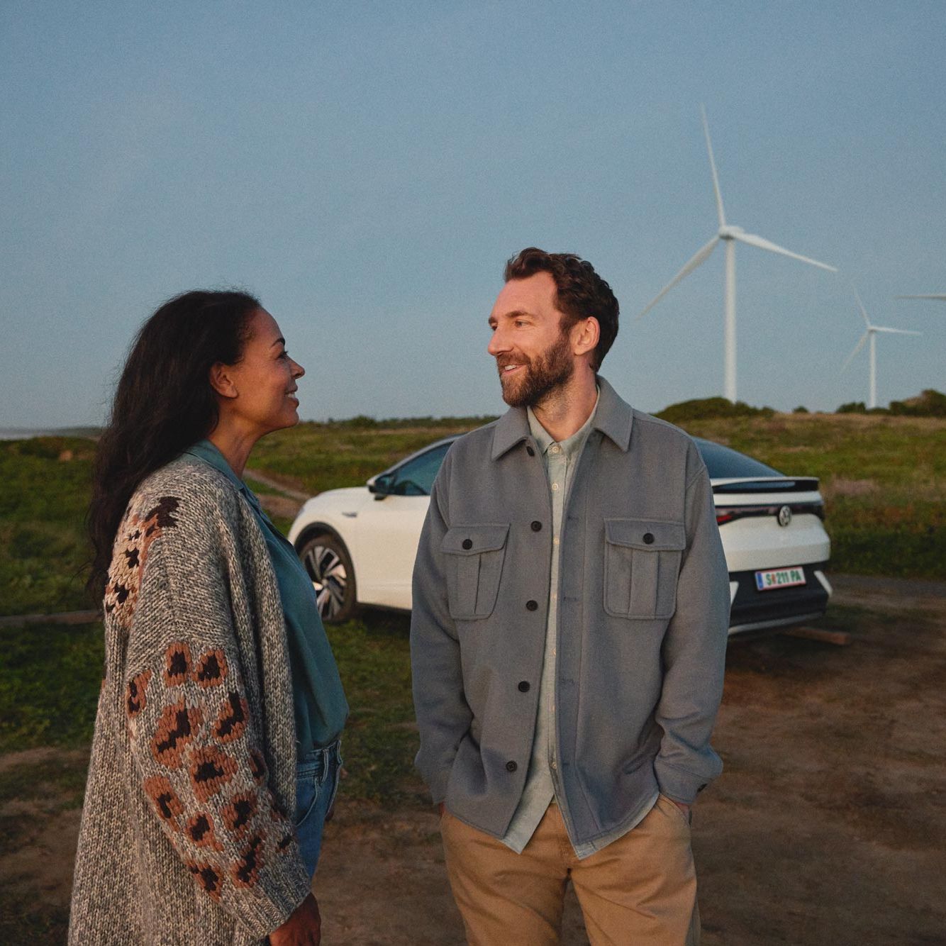 Volkswagen Way to Zero Eine Frau und ein Mann stehen vor einem weißen ID.5 und schauen sich gegenseitig an.