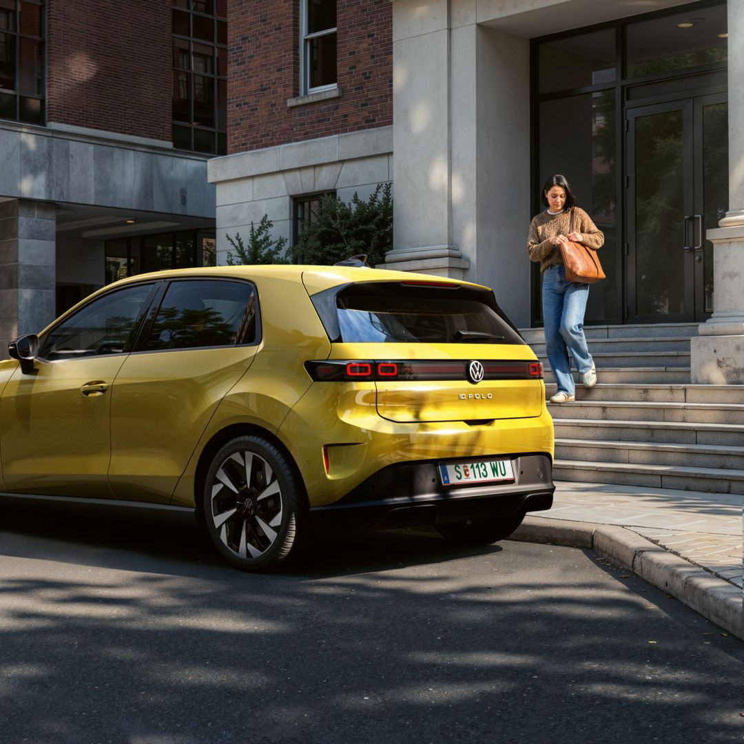 VW ID. Polo Trend v barvi Python Yellow Metallic v 3/4 zadnjem pogledu, parkiran na mestni ulici pred stanovanjskimi stavbami.