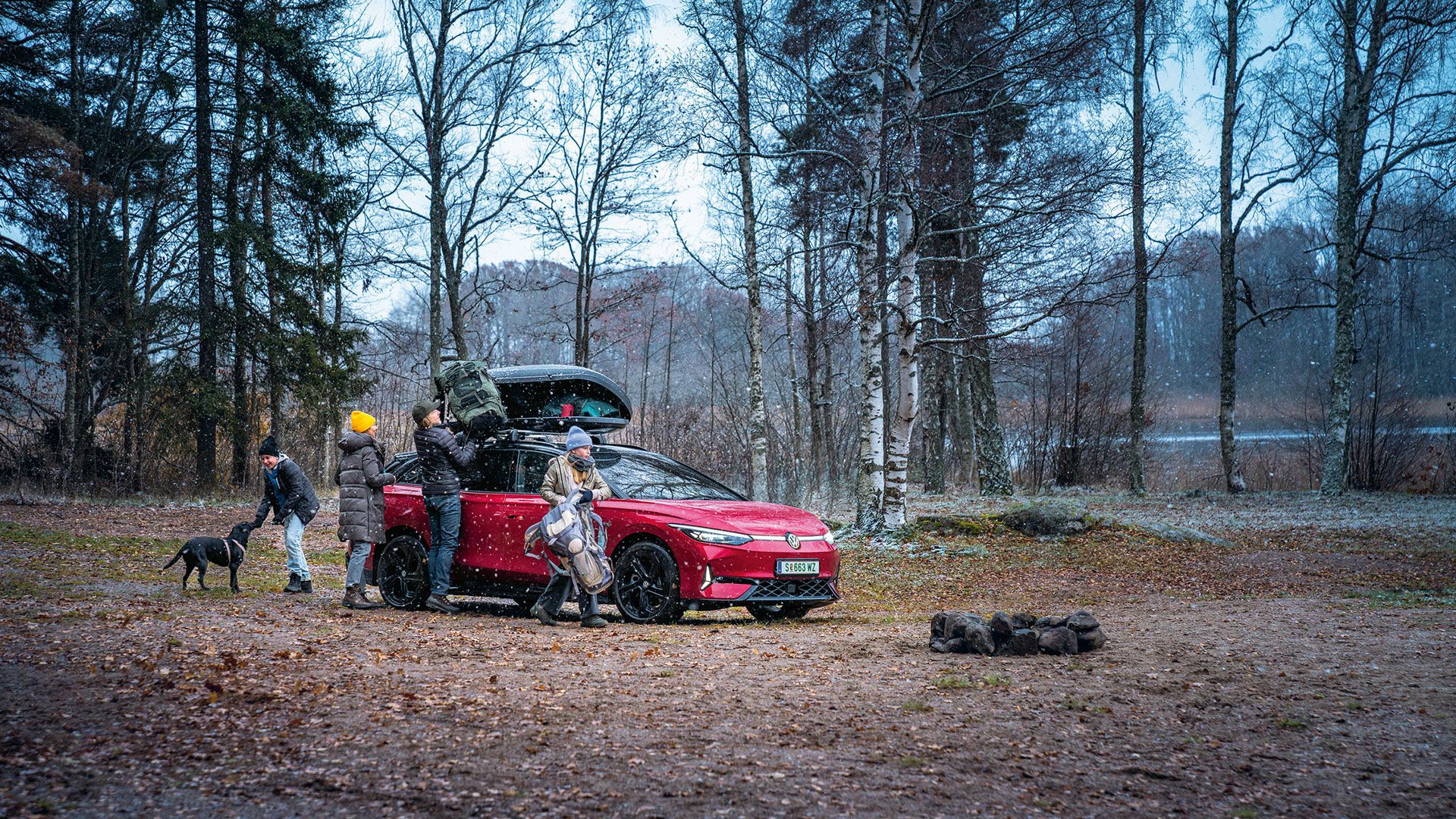 VW ID.7 GTX Tourer s strešnim kovčkom, družina raztovarja prtljago.
