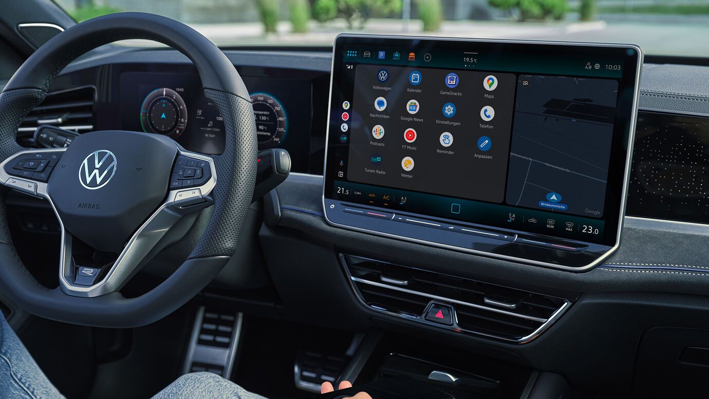 Detajlni posnetek armaturne plošče v VW Passatu. Oseba na voznikovem sedežu drži v roki pametni telefon.