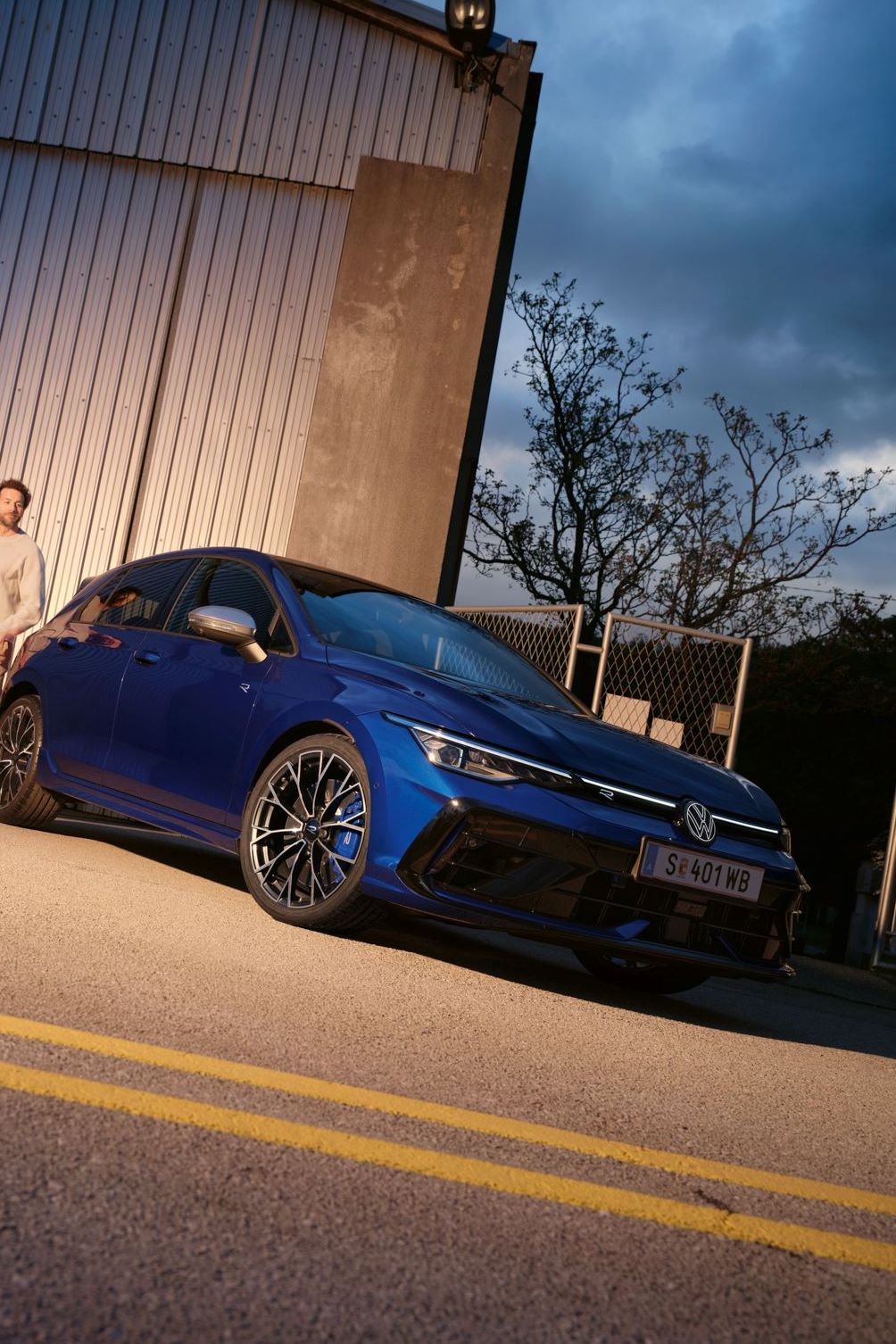 Ein roter VW Golf GTI steht vor einem Gebäude. Zwei Personen sitzen neben dem Wagen.