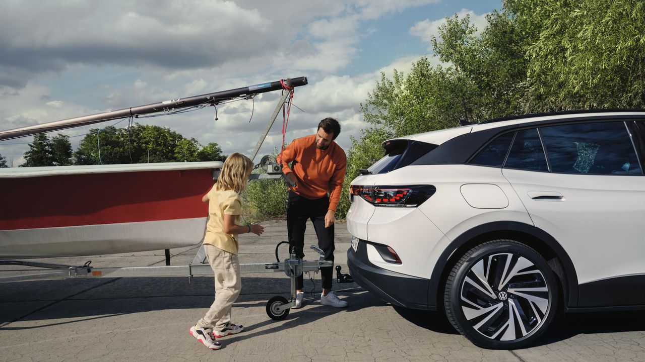 Stranska silhueta belega VW ID.4, moški in deklica na vlečno kljuko priklapljata prikolico s čolnom.