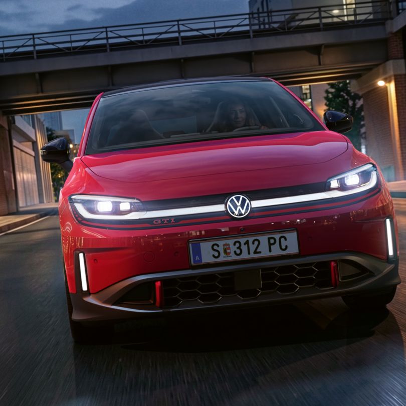 Oseba zvečer vozi rdeč VW ID. Polo GTI skozi sodobno osvetljeno poslovno četrt.