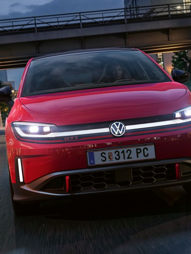 Oseba zvečer vozi rdeč VW ID. Polo GTI skozi sodobno osvetljeno poslovno četrt.
