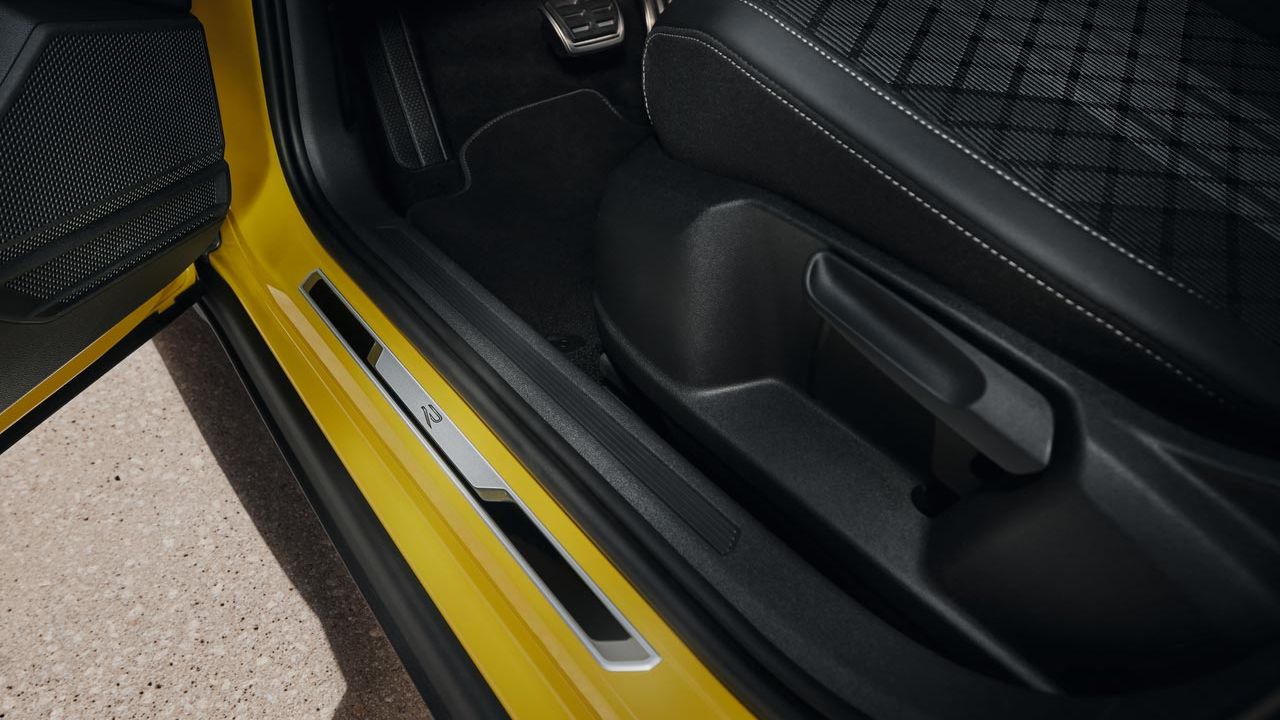 Sprednja vrata rumenega VW T-Crossa so odprta in videti je mogoče spodnji del voznikovega sedeža in vstopno letev iz krtačenega legiranega jekla.