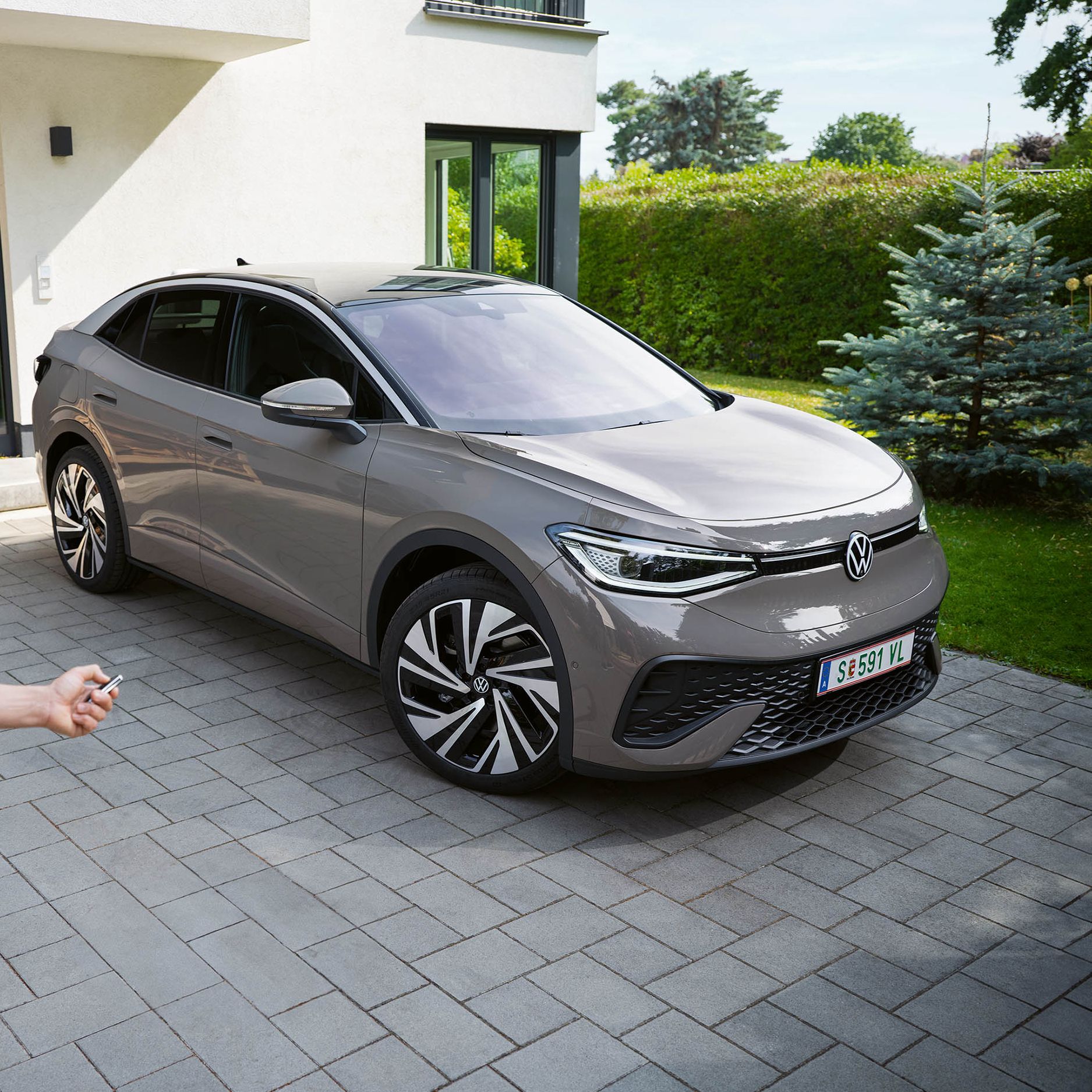 Ein grauer ID.5 steht in einer Einfahrt vor einem Haus, ein Mann schließt das Auto ab. 