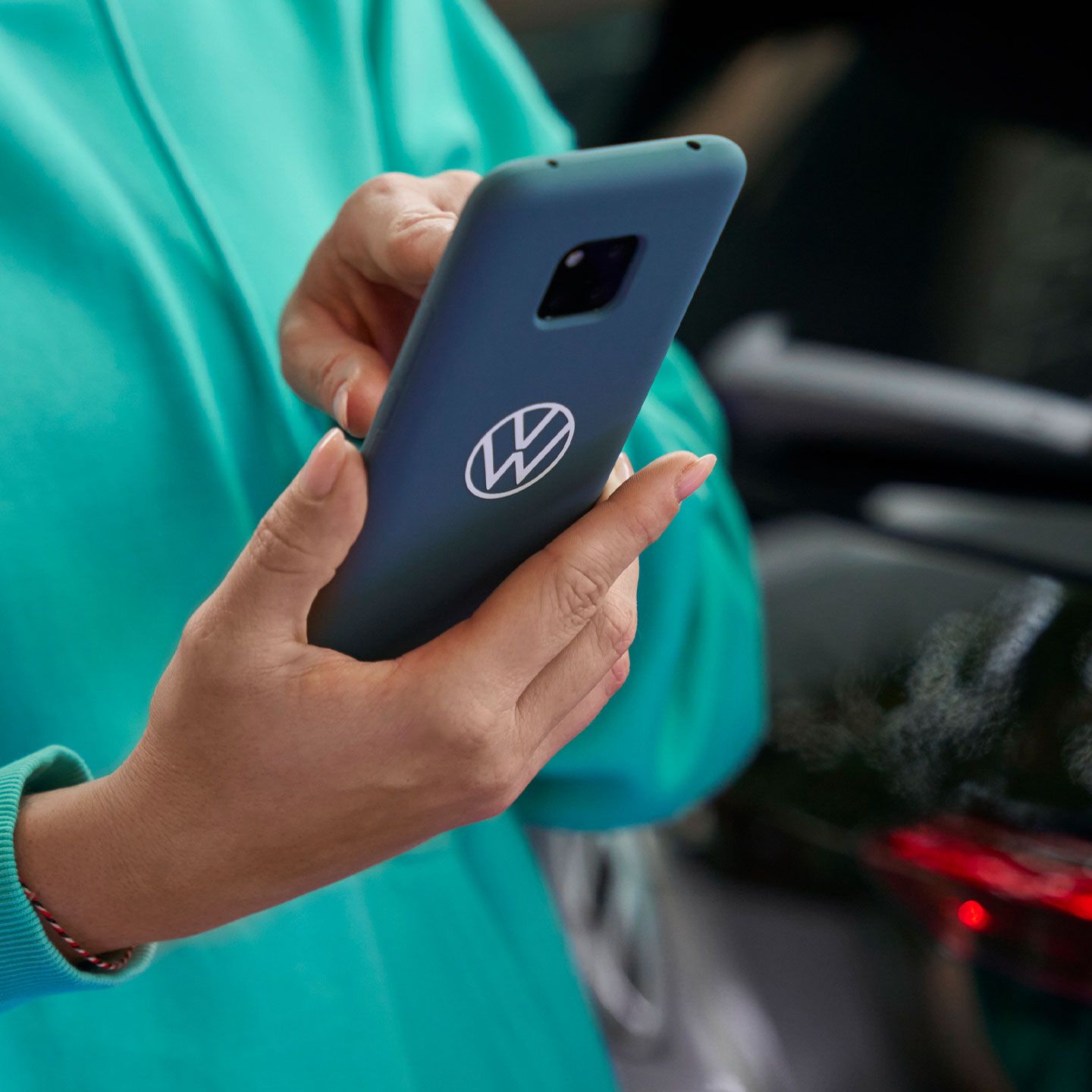 Ženska drži svoj pametni telefon. V ozadju je Volkswagen ID.3.