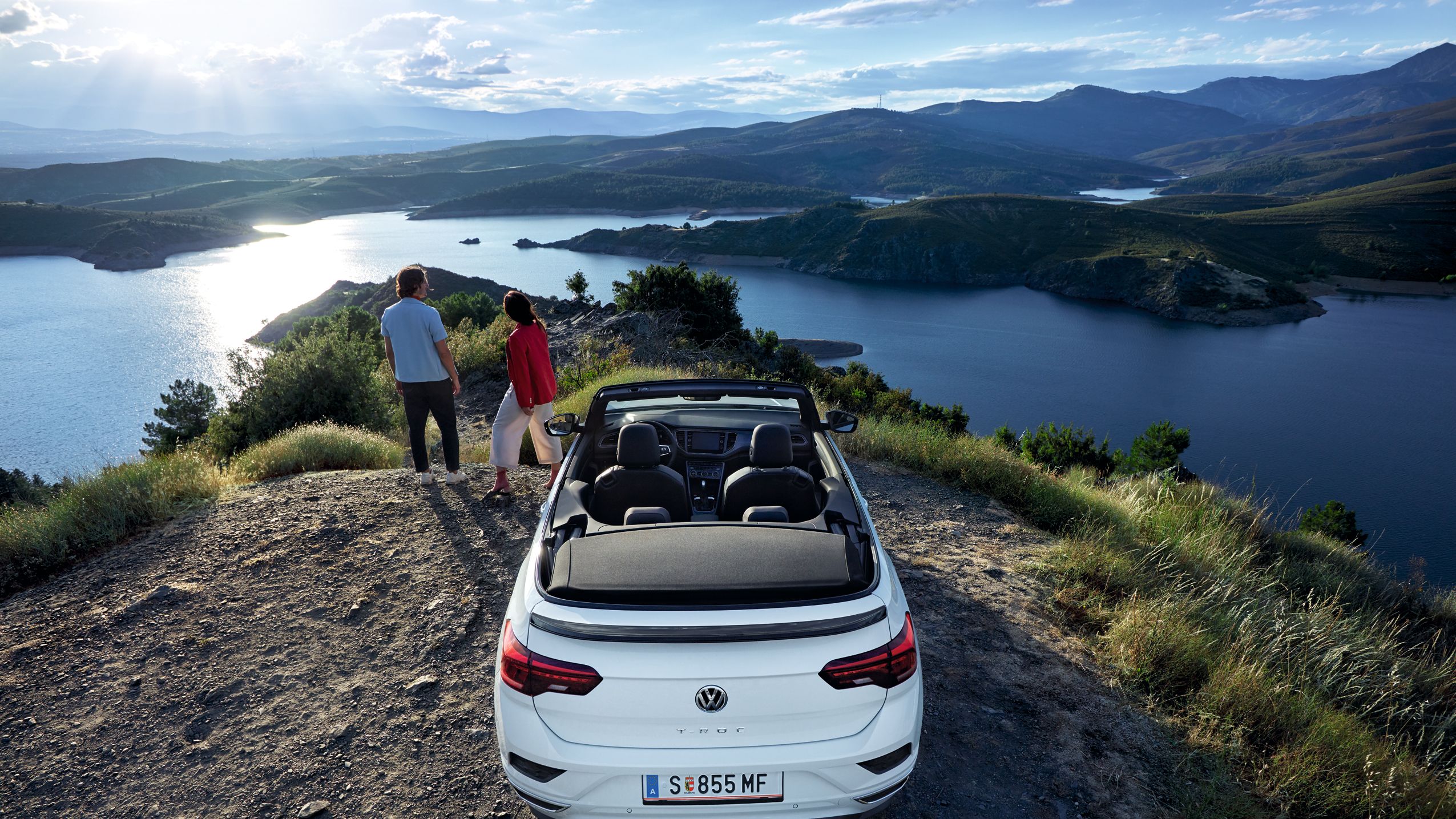 VW T-Roc Cabriolet pred čudovitim razgledom, par stoji poleg avtomobila