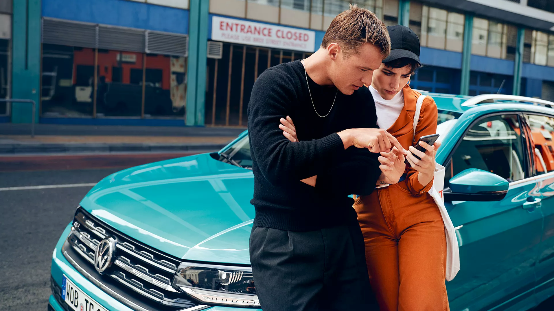 Moški in ženska se naslanjata na parkirani VW T-Cross in skupaj gledata na mobilni telefon