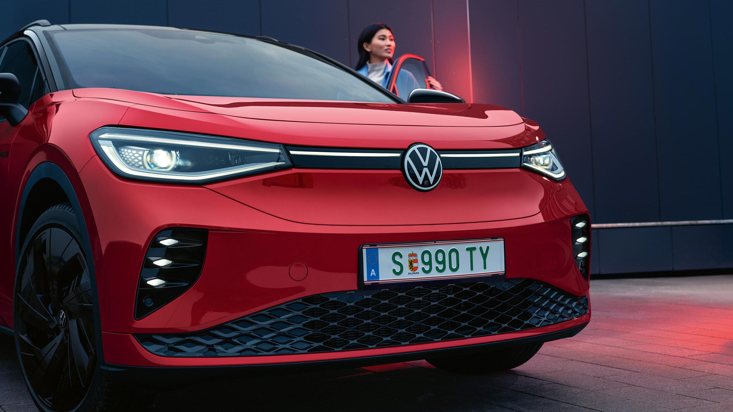 VW ID.4 GTX in Rot mit geöffneter Fahrertür. Frau steht an der Tür und guckt nach vorne.