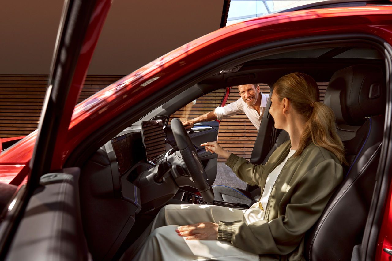 Ženska sedi na voznikovem sedežu Tiguana in gleda v navigacijski sistem. Moški gleda skozi odprta sovoznikova vrata.