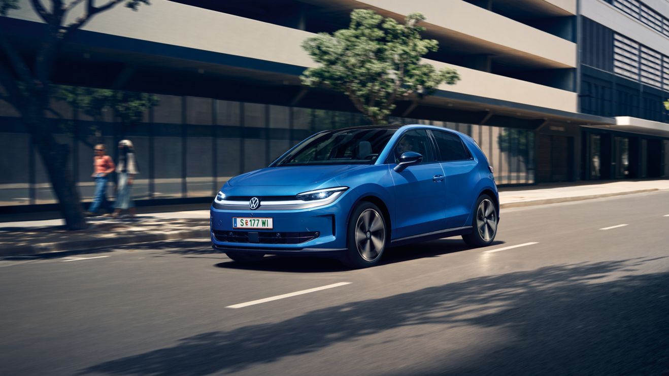 Moder VW ID. Polo Style vozi skozi mesto z zelenimi drevesi ob cesti.