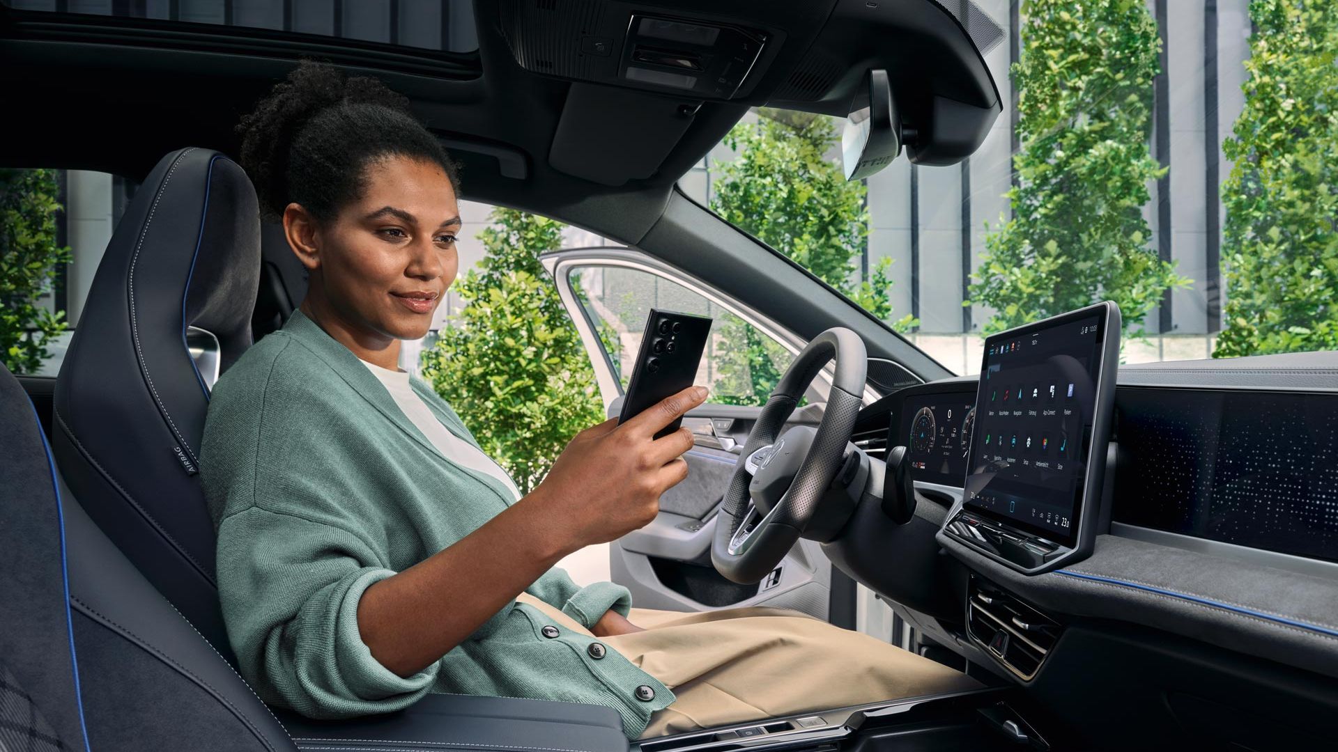 Bel VW Passat je parkiran bočno pred stavbo. Pogled od zadaj na žensko, ki gleda v svoj pametni telefon.