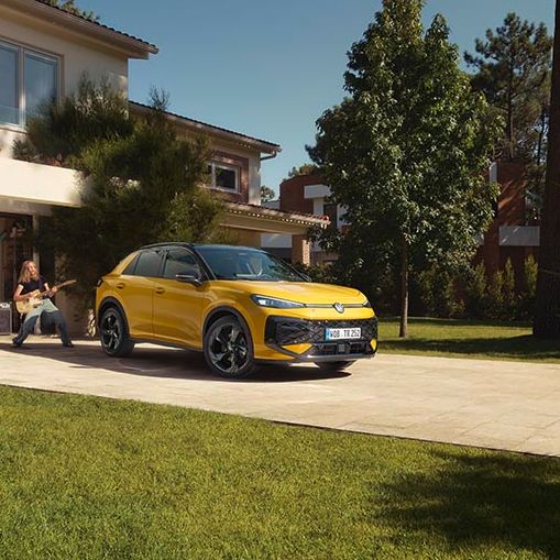 Rumeni VW T-Roc je parkiran pred moderno hišo z lepo urejenim dvoriščem in zelenico. 