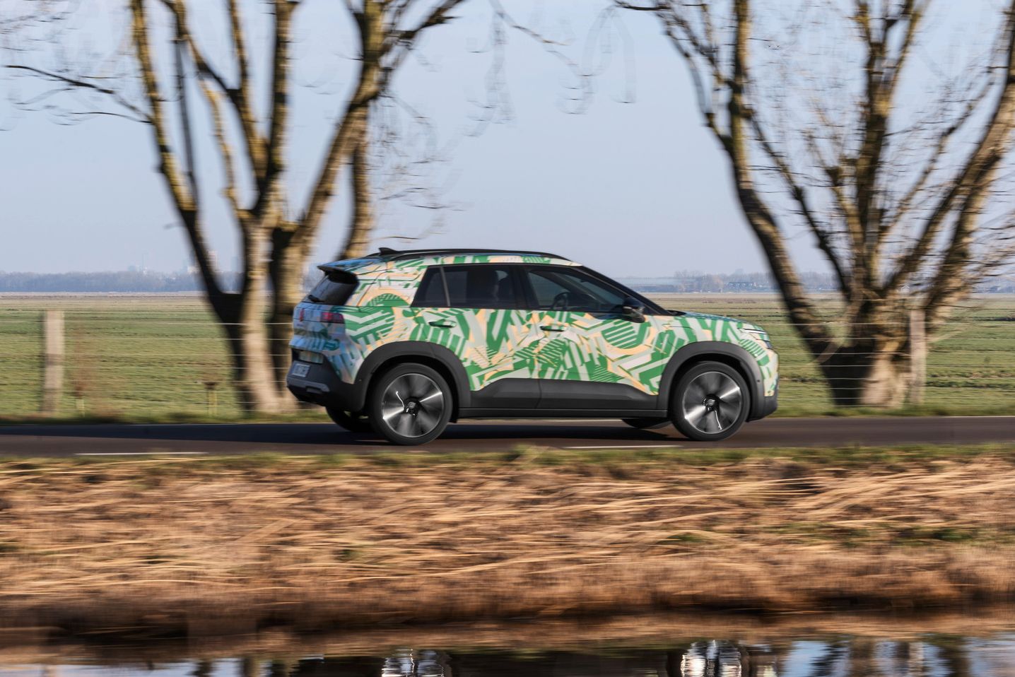 VW ID. Cross z maskirno folijo je od strani prikazan med vožnjo po regionalni cesti.