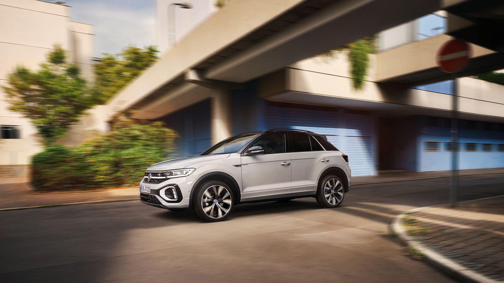 Bel VW T-Roc R-Line med dinamično vožnjo čez križišče, pogled s strani.