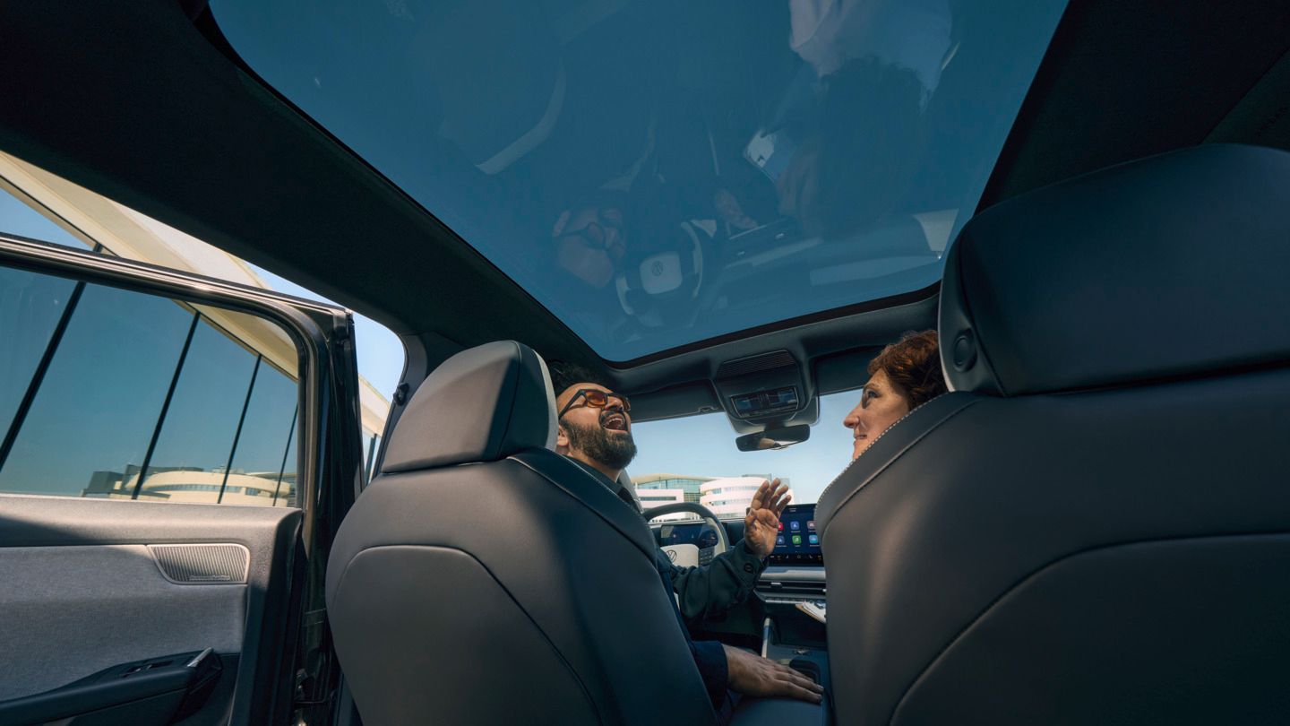 Nasmejan moški sedi na voznikovem sedežu v VW ID. Crossu in gleda skozi odprto panoramsko strešno okno.