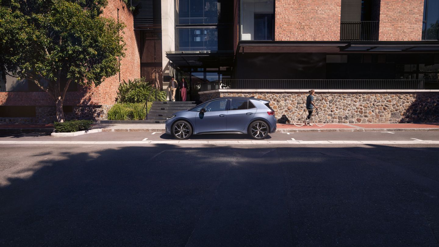 Modri VW ID.3 Neo je parkiran pred stanovanjsko stavbo, iz katere prihajata ženska in moški.