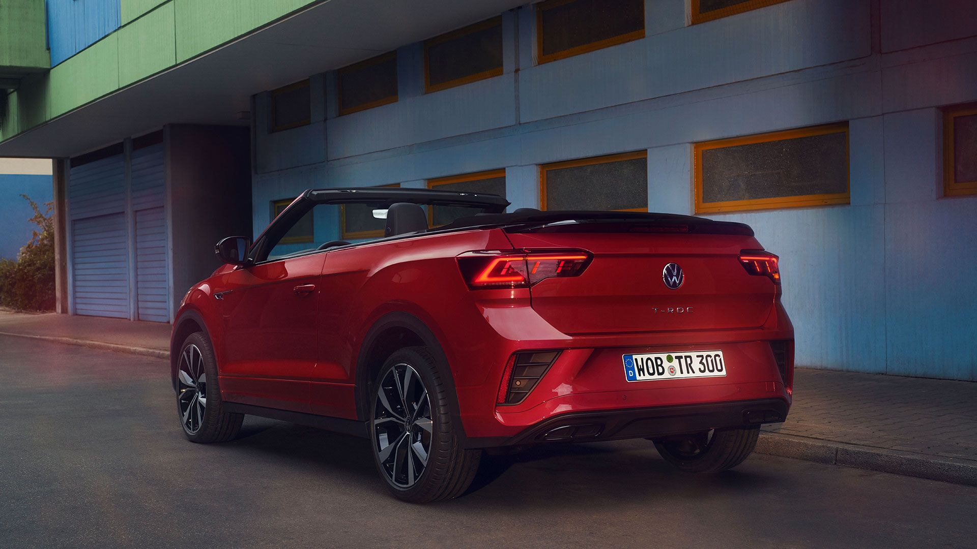 Pogled na zadek rdečega T-Roc Cabrioleta z odprto streho, parkiranega ob robu cestišča. 