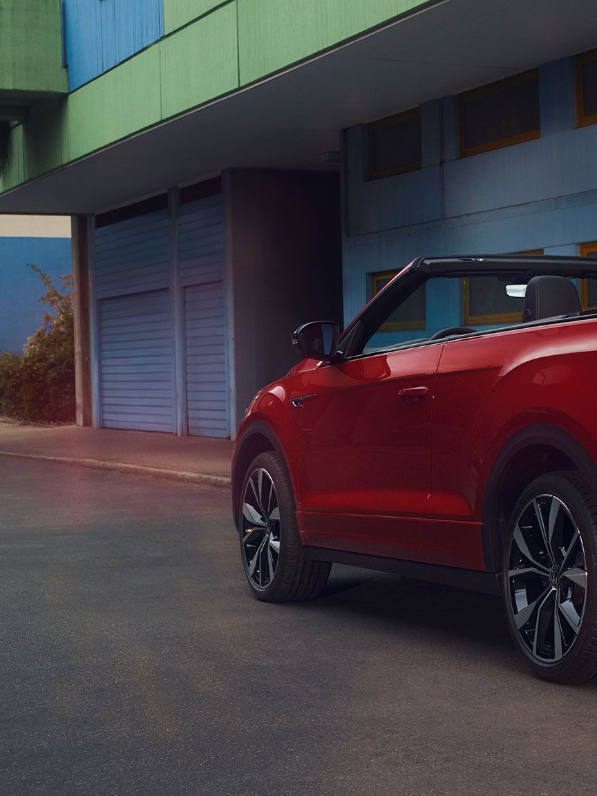 Pogled na zadek rdečega T-Roc Cabrioleta z odprto streho, parkiranega ob robu cestišča. 