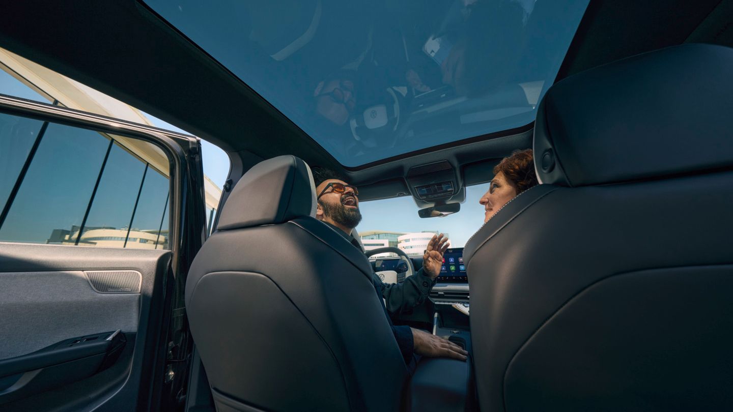 Nasmejan moški sedi na voznikovem sedežu v VW ID. Crossu in gleda skozi odprto panoramsko strešno okno.