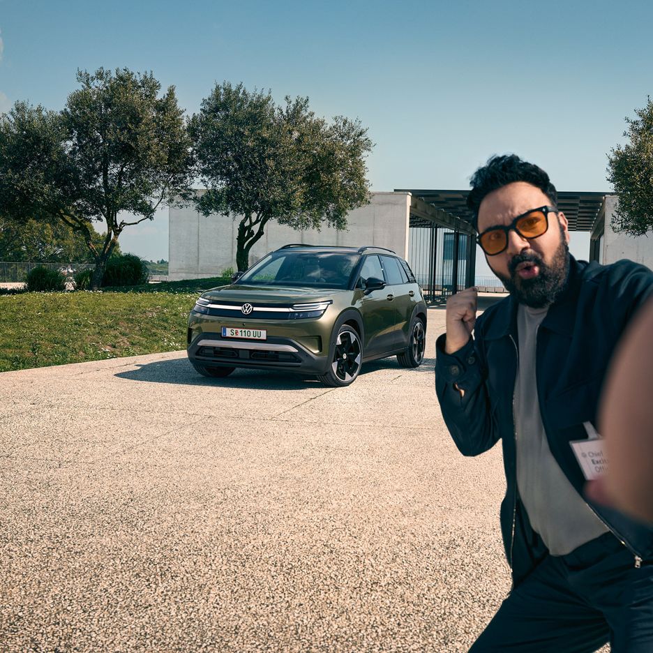 Moški naredi selfi z zelenim VW ID. Cross-om parkiran na dovozu stavbe.
