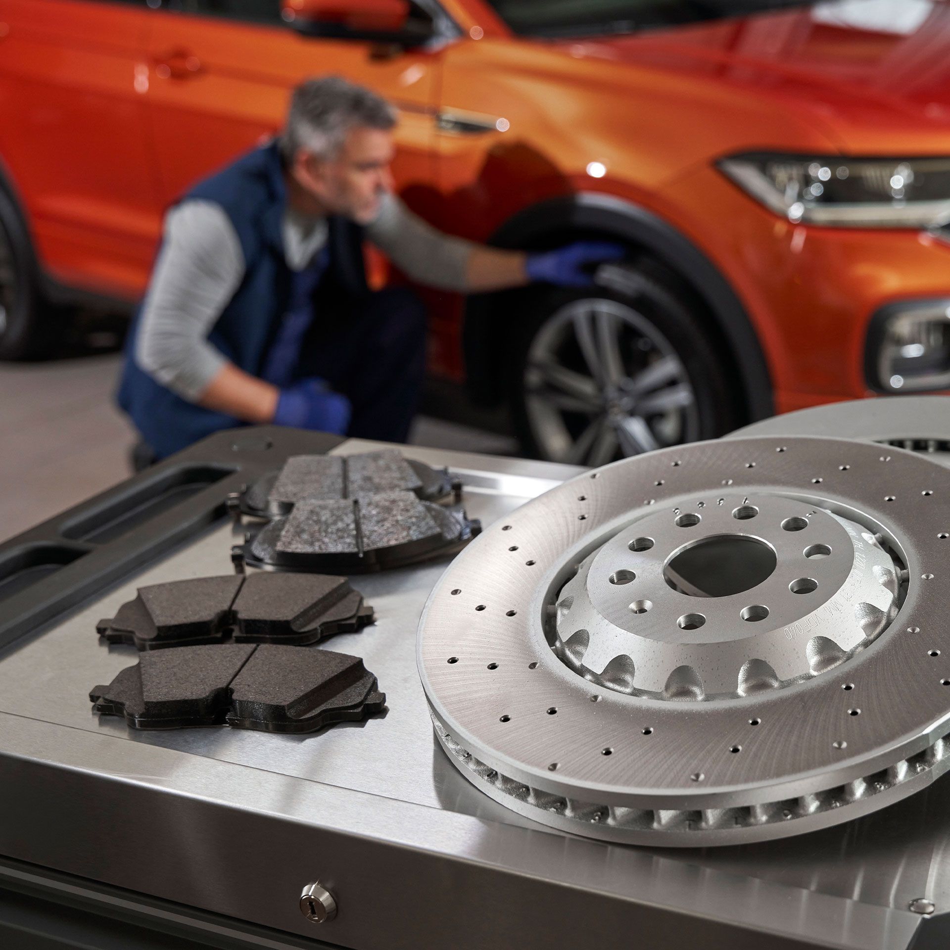 Avto mehanik pregleduje gumo na VW T-Roc, v ospredju pa so zavorni diski in obloge.