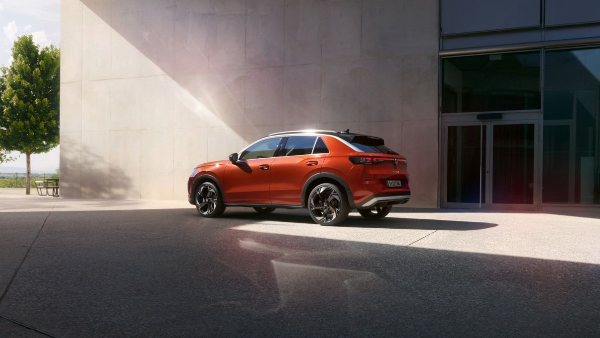 Oranžen VW T-Roc je parkiran pred sodobno stavbo z velikimi steklenimi površinami. 