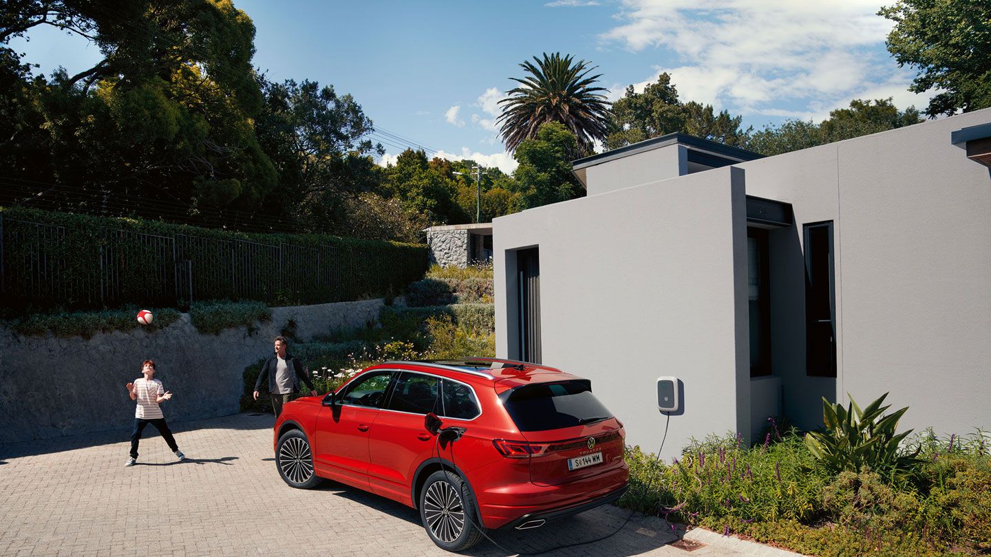 VW Touareg Elegance eHybrid, pogled poševno od zadaj, na polnilnem mestu pred sodobno hišo.