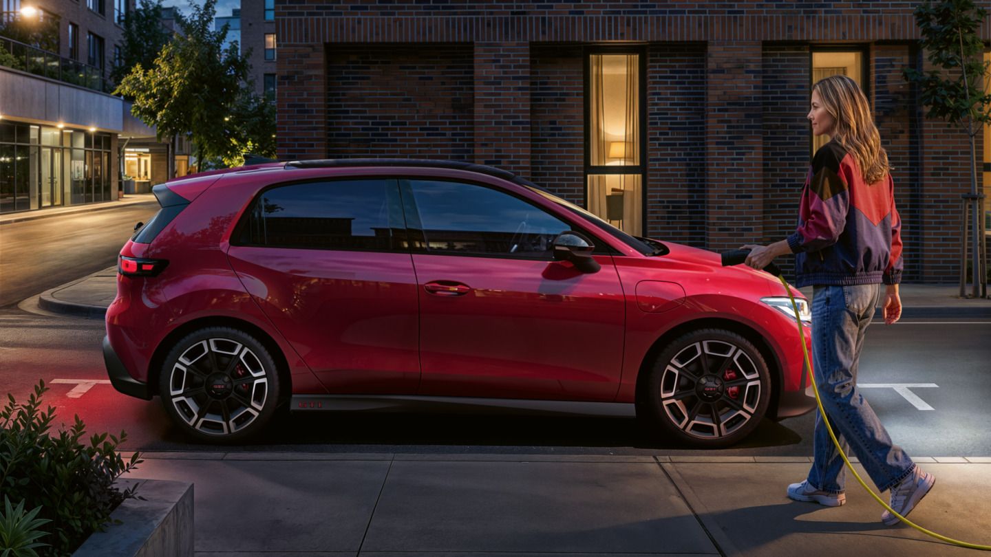 Oseba se približa rdečemu VW ID-ju. Polo GTI, parkiran ob strani z DC polnilnim kablom.