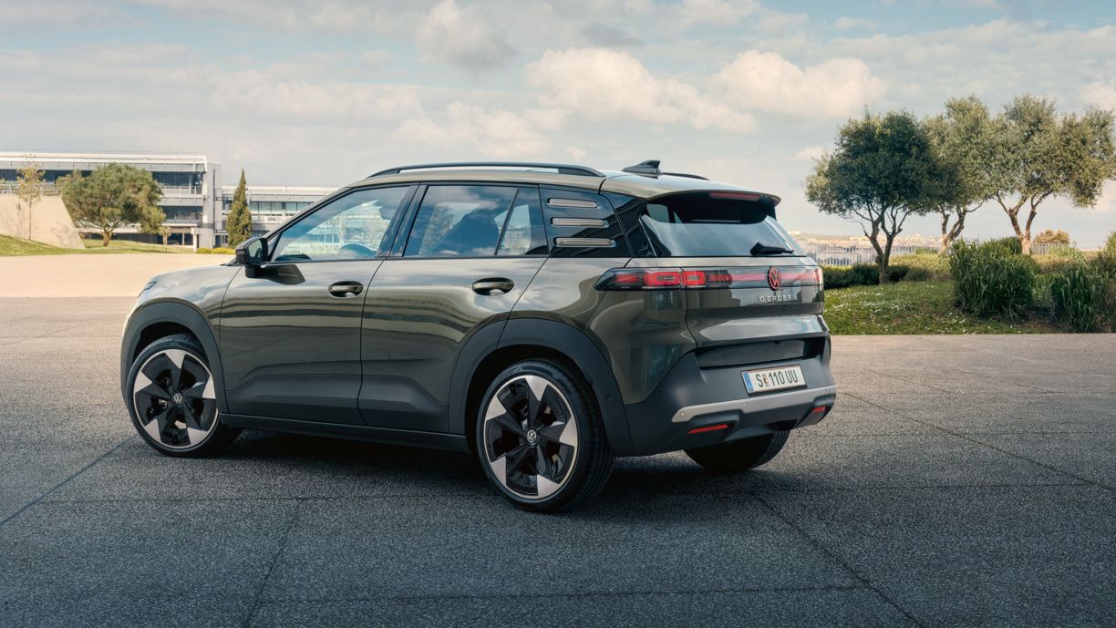 Pogled na zadek zelenega VW ID. Crossa, ki stoji na trgu z zelenimi drevesi. 