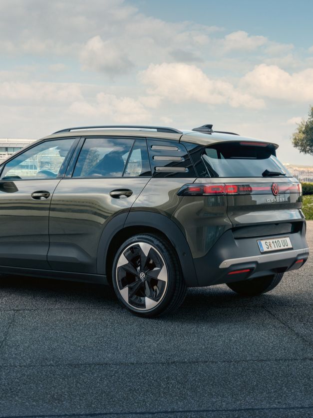 Pogled na zadek zelenega VW ID. Crossa, ki stoji na trgu z zelenimi drevesi. 