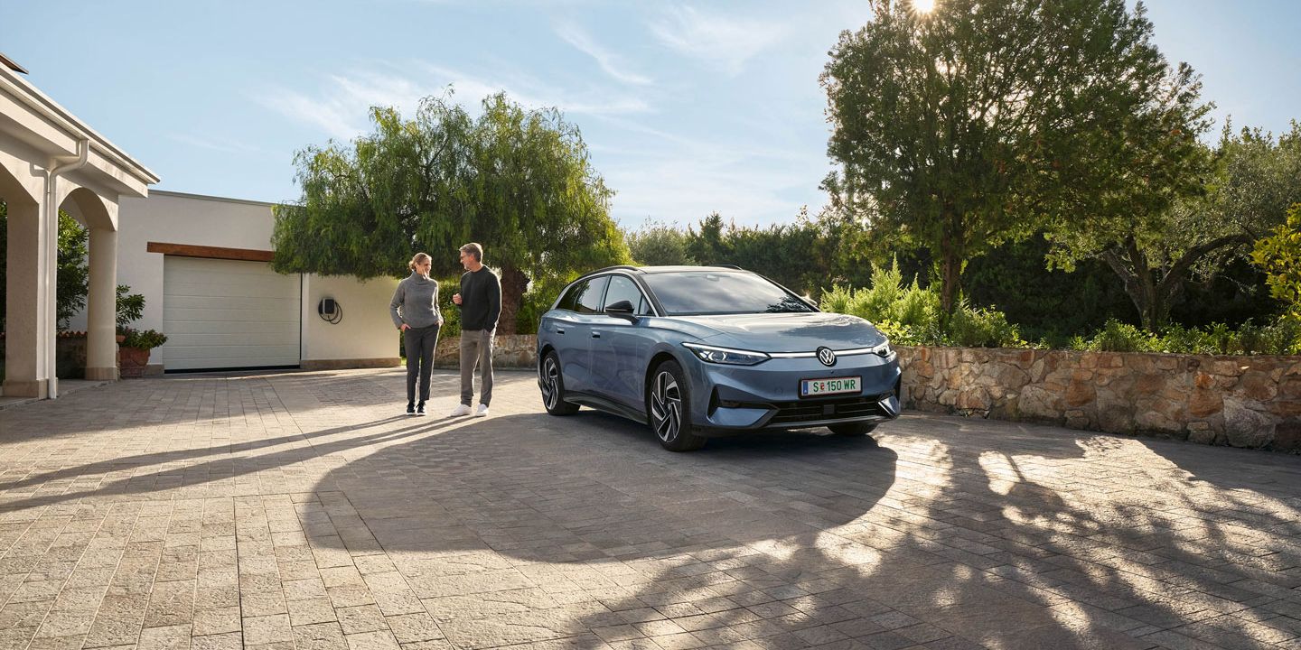 Der VW ID.7 Tourer ist vor Einfamillienhaus geparkt, eine Frau und ein Mann stehen neben ihm und unterhalten sich