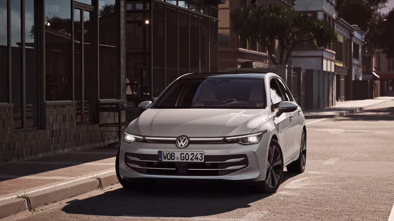 "Bel VW Golf se pelje po cesti proti križišču. "