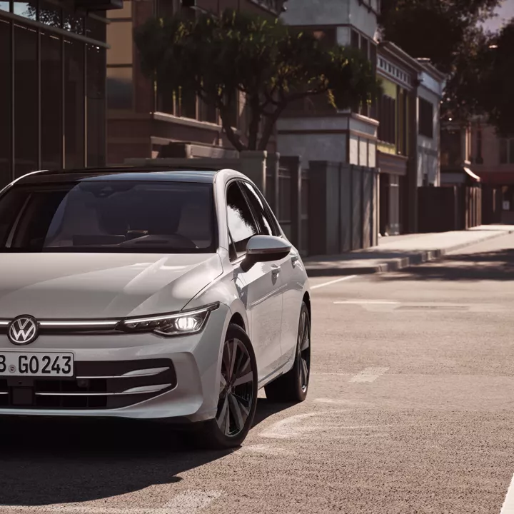 "Bel VW Golf se pelje po cesti proti križišču. "