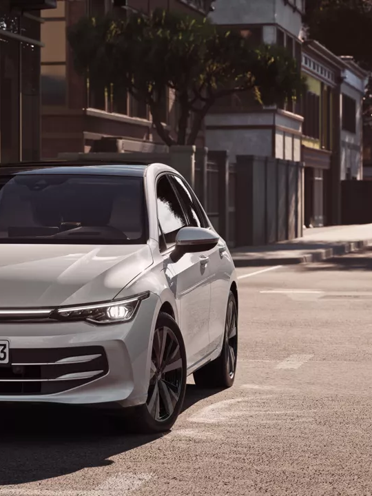 "Bel VW Golf se pelje po cesti proti križišču. "