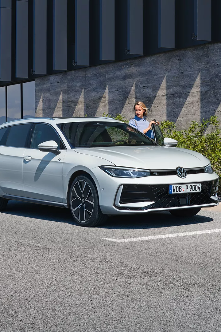 VW Passat in weiß parkt seitlich vor einem Gebäude.