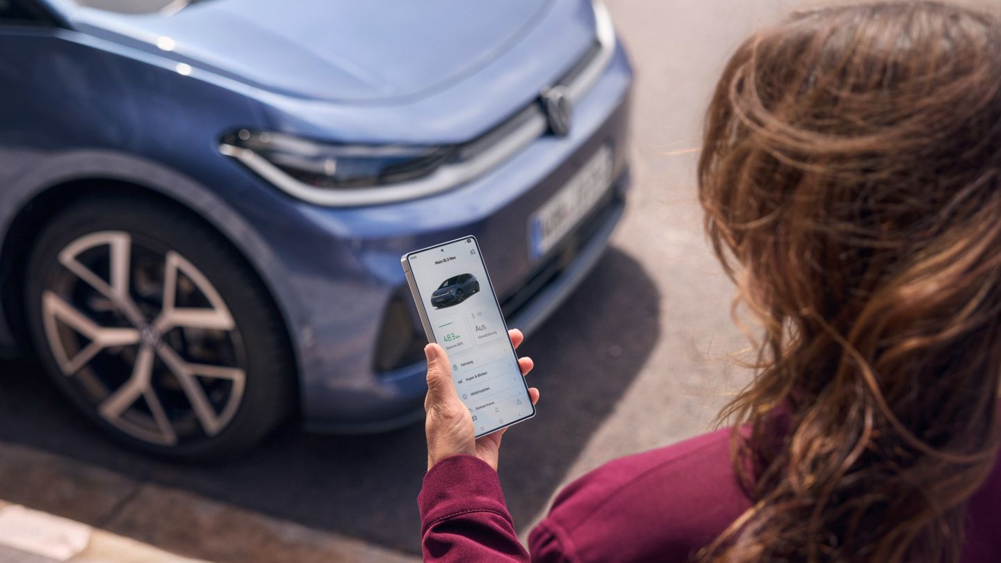 Ženska pogleda na svoj pametni telefon, pred njo je parkiran moder VW ID.3 Neo
