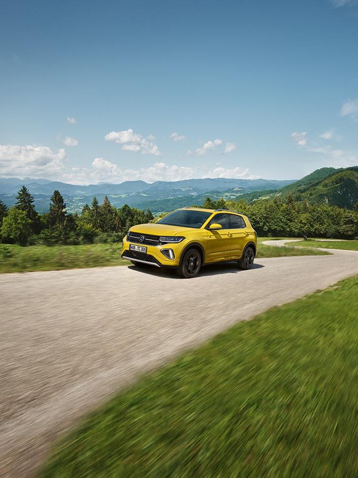 Rumen VW T-Cross na cesti sredi hribovite pokrajine.
