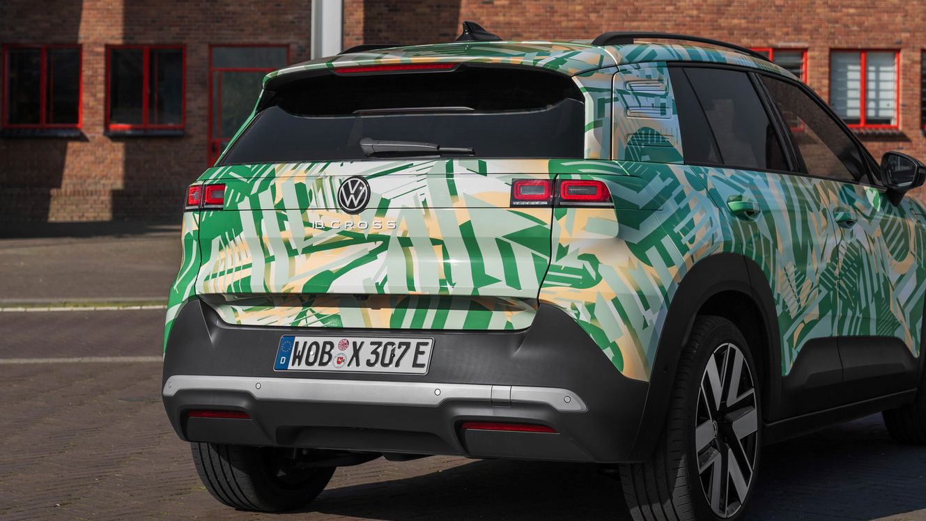 Volkswagen SUV je parkiran pred opečnato stavbo. Avto ima zeleno in belo kamuflažno barvo. Vidna je od zadaj in tudi od strani.