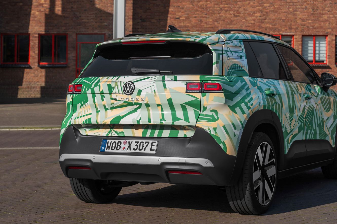 Volkswagen SUV je parkiran pred opečnato stavbo. Avto ima zeleno in belo kamuflažno barvo. Vidna je od zadaj in tudi od strani.