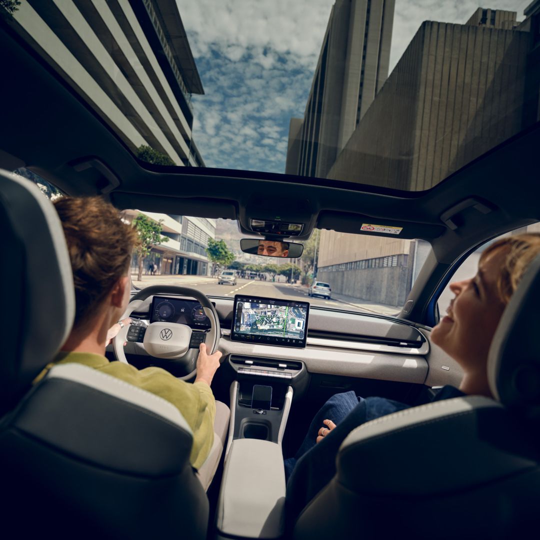 Moški vozi VW ID. Polo Style, na sovoznikovem sedežu ženska, ki se smeji. Visoke stavbe so vidne skozi panoramsko streho