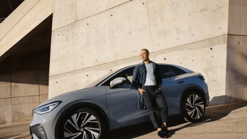 Stranska silhueta sivega VW ID.5, ki je parkiran pred svetlo steno. Moški se naslanja na voznikova vrata.