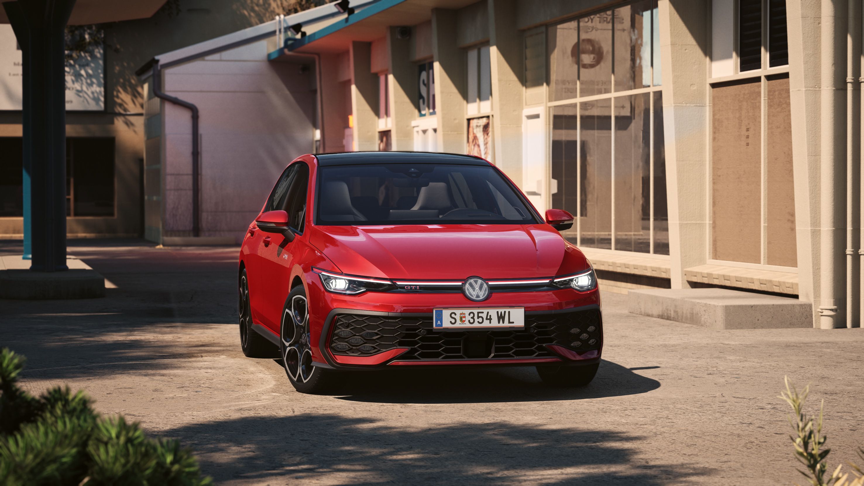 Od spredaj je prikazan rdeč VW Golf GTI, ki se pelje mimo stavbe.